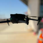 Drone flying in the foreground at a construction site in Queen Creek, with the company founder wearing safety gear in the background.